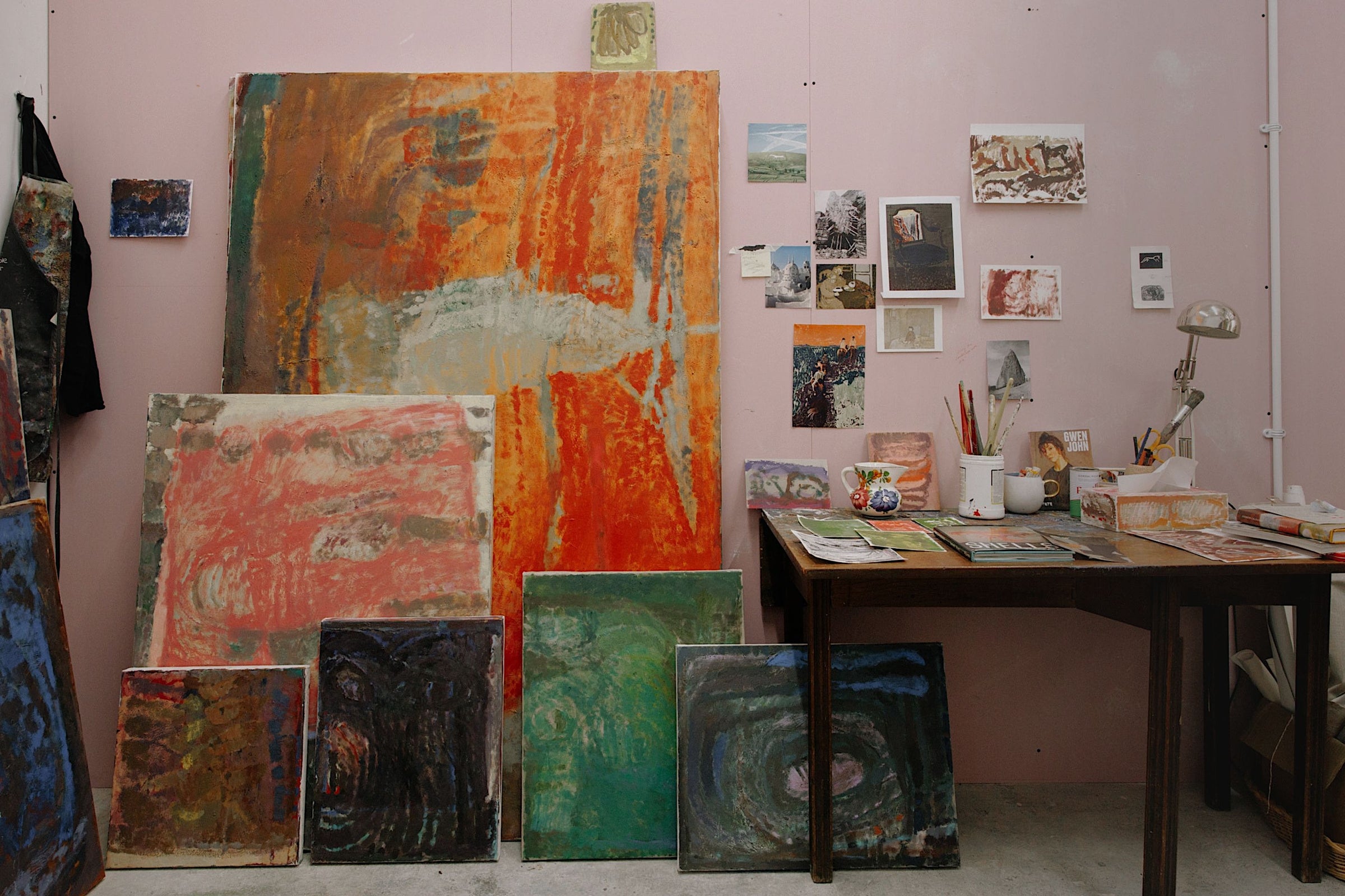 Large canvas paintings leaning against Katarina Lalic's studio wall next to a workspace desk covered in notes and visual references, featured for the Partnership Editions Statement Artworks Art Edit collection.