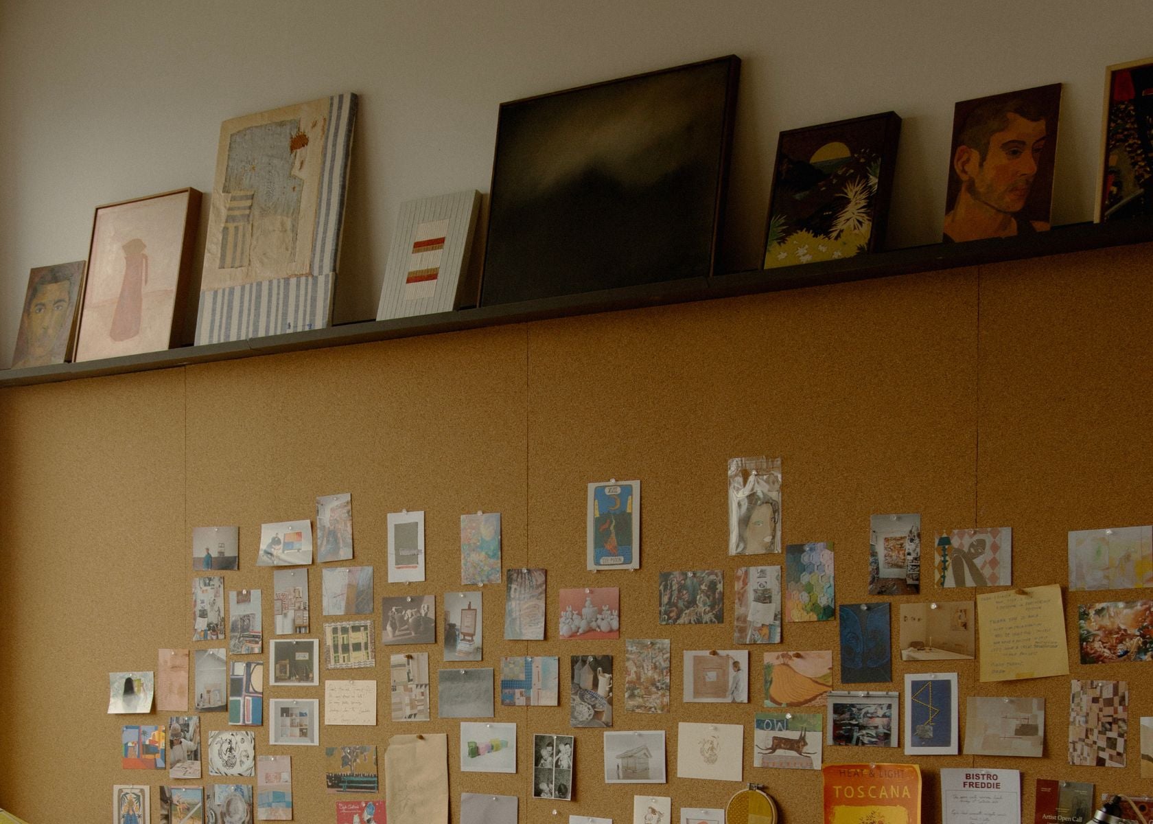 A detailed close-up of a shelf above a desk space, displaying a curated selection of small-scale original artworks and from consigned artists on the Partnership Editions studio artworks page.