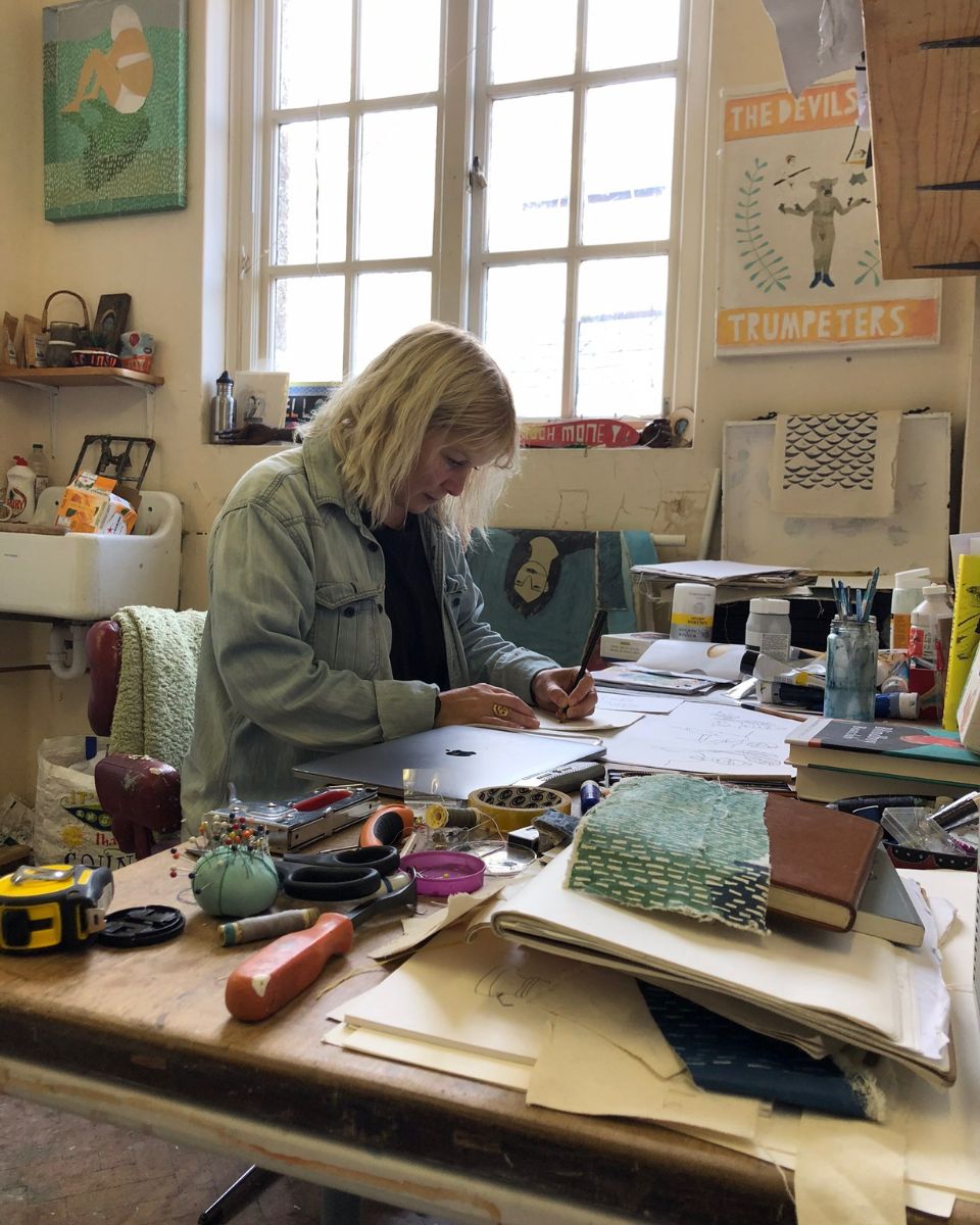 Artist Ali Bassett annotating ideas and sketches amongst original artwork inside her Cornwall art studio.