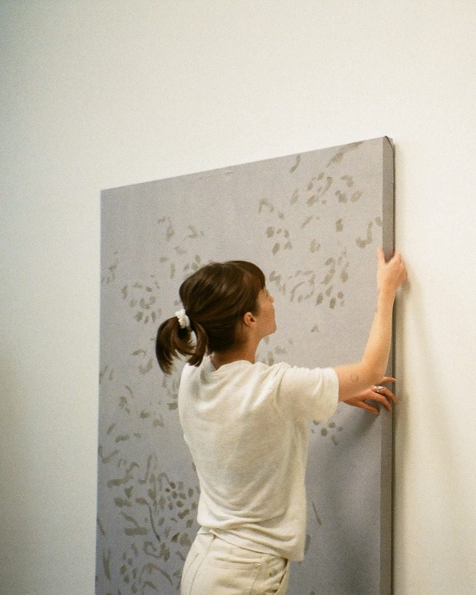 Artist Alina Welch hanging a large original canvas painting on a wall inside her art studio.