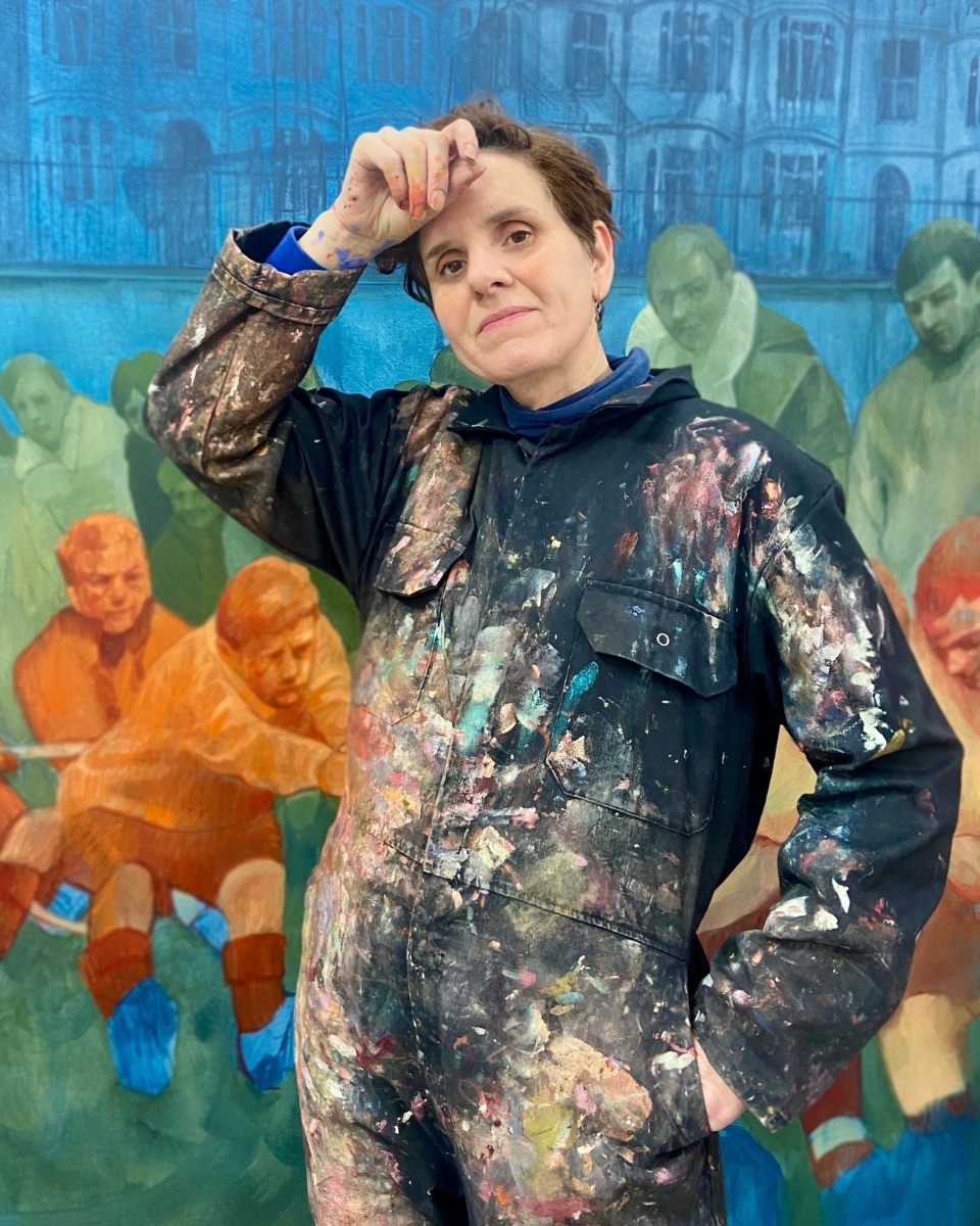Figurative painter Amy Dury in her studio, wearing a boiler suit in front of a large-scale oil canvas.