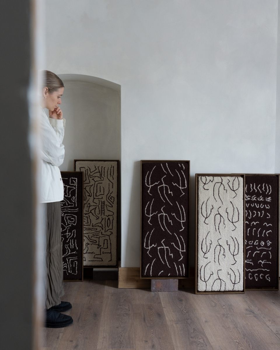 Carousel image of artist Bec Kirby alongside a series of framed tufted artworks in her studio for Partnership Editions.