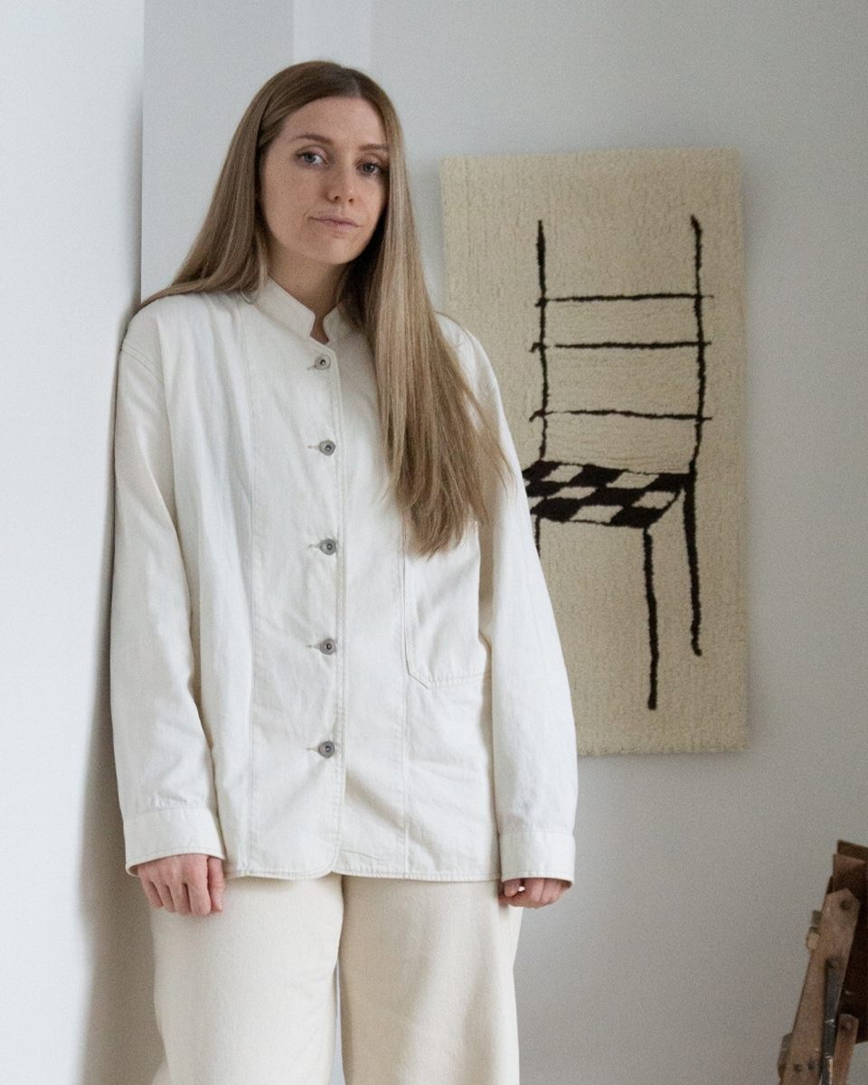 Textile artist Bec Kirby posing in her studio in front of a heavily textured tufted wall artwork.