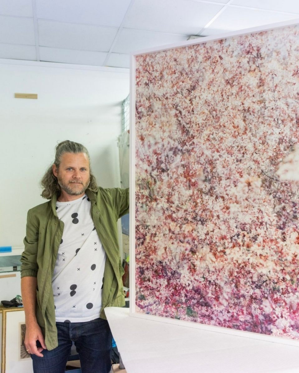 Photographer Casey Moore posing in front of a framed, large-scale analogue botanical photograph.