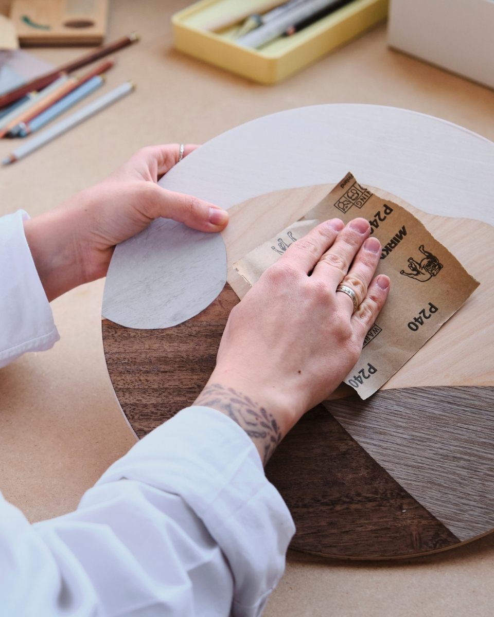 Close-up image of Chelsea Vivash’s hands sanding a contemporary wood-veneer artwork in her artist studio for Partnership Editions.