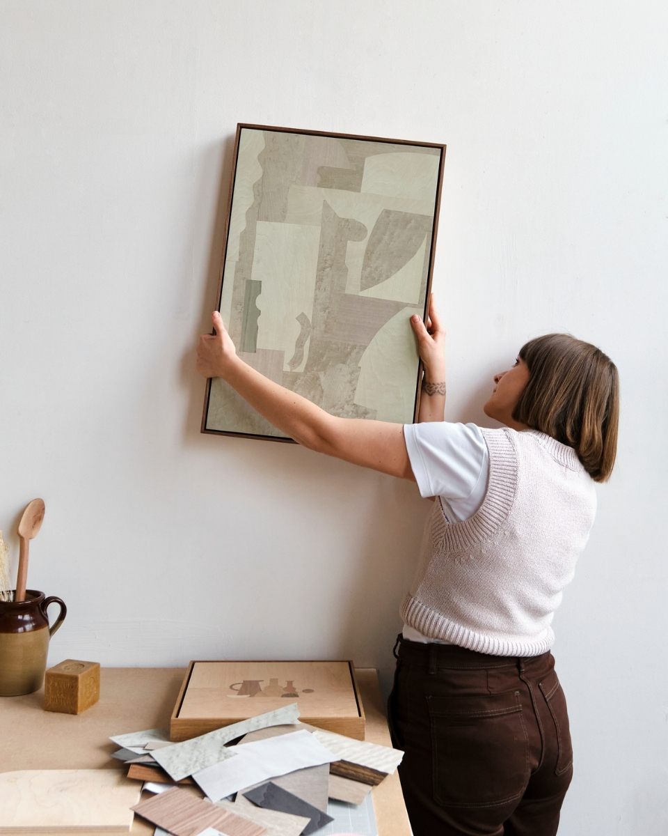 Carousel image of Chelsea Vivash mounting a framed contemporary wood-veneer artwork in her studio for Partnership Editions.