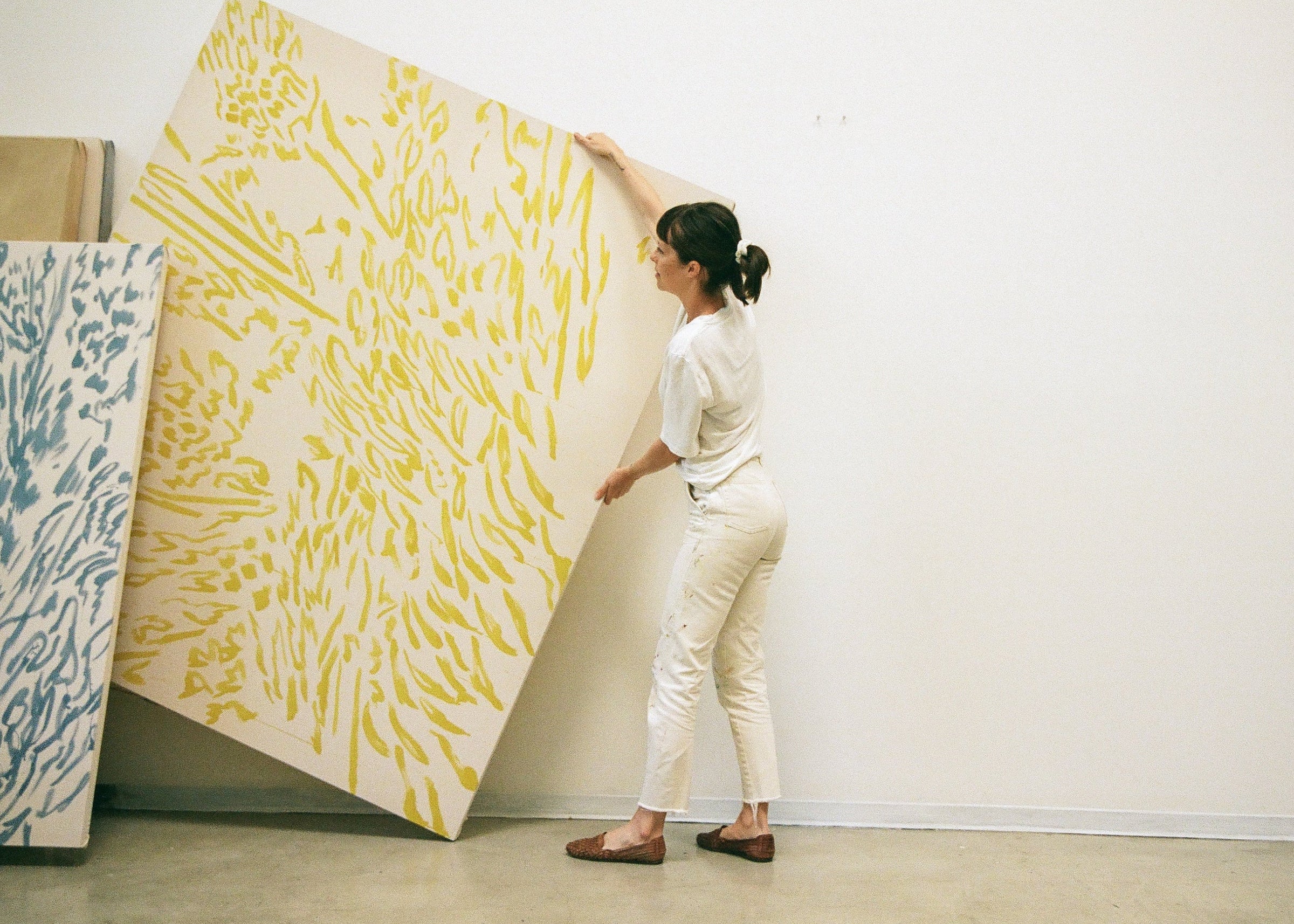 Artist Alina Welch moving one of her large-scale abstract paintings inside her studio space, featured as the introduction image for the Partnership Editions FAQ section.