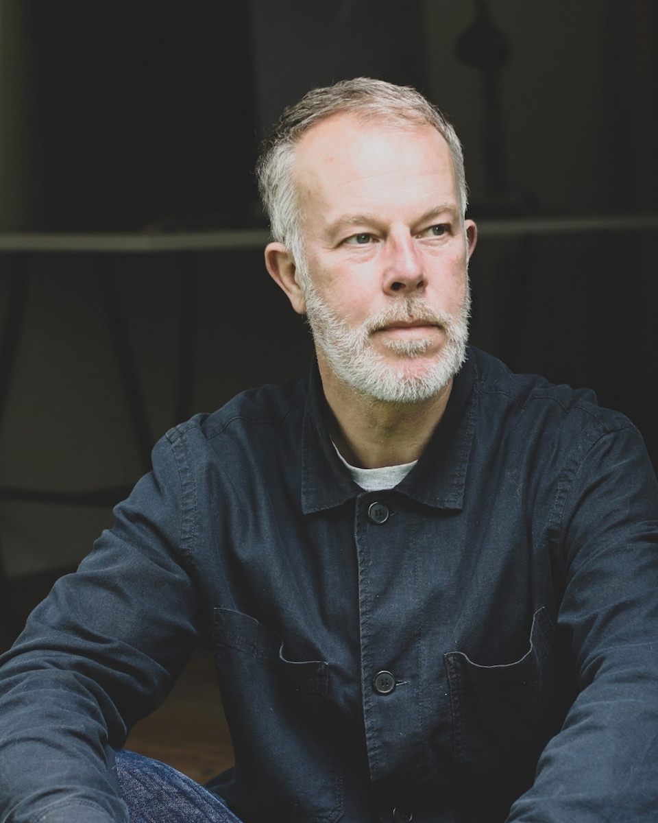 Portrait of artist David Hardy sitting at the entrance of his West Wales studio for Partnership Editions.