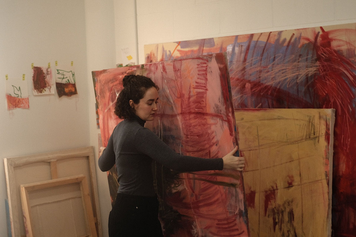 Artist Ellie Walker moving a large pink and red abstract canvas inside her studio for Partnership Editions.