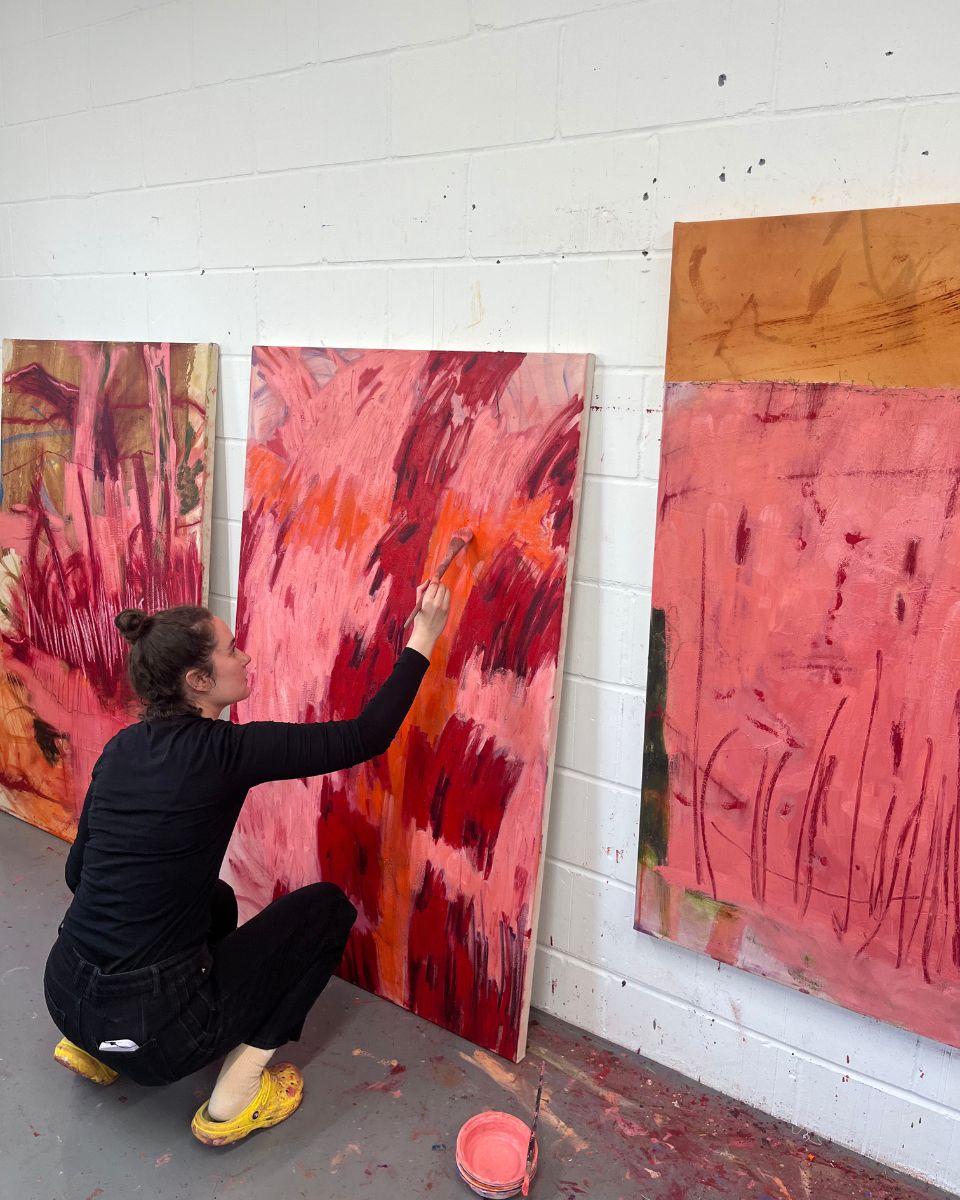 Artist Ellie Walker applying thick red and orange paint to a large abstract canvas in her studio.