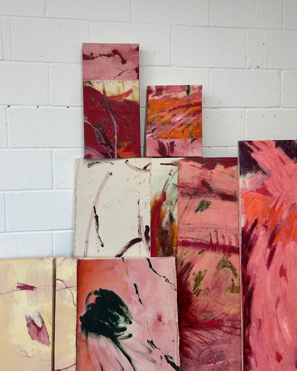 Selection of small and medium abstract oil paintings stacked against a white brick studio wall.