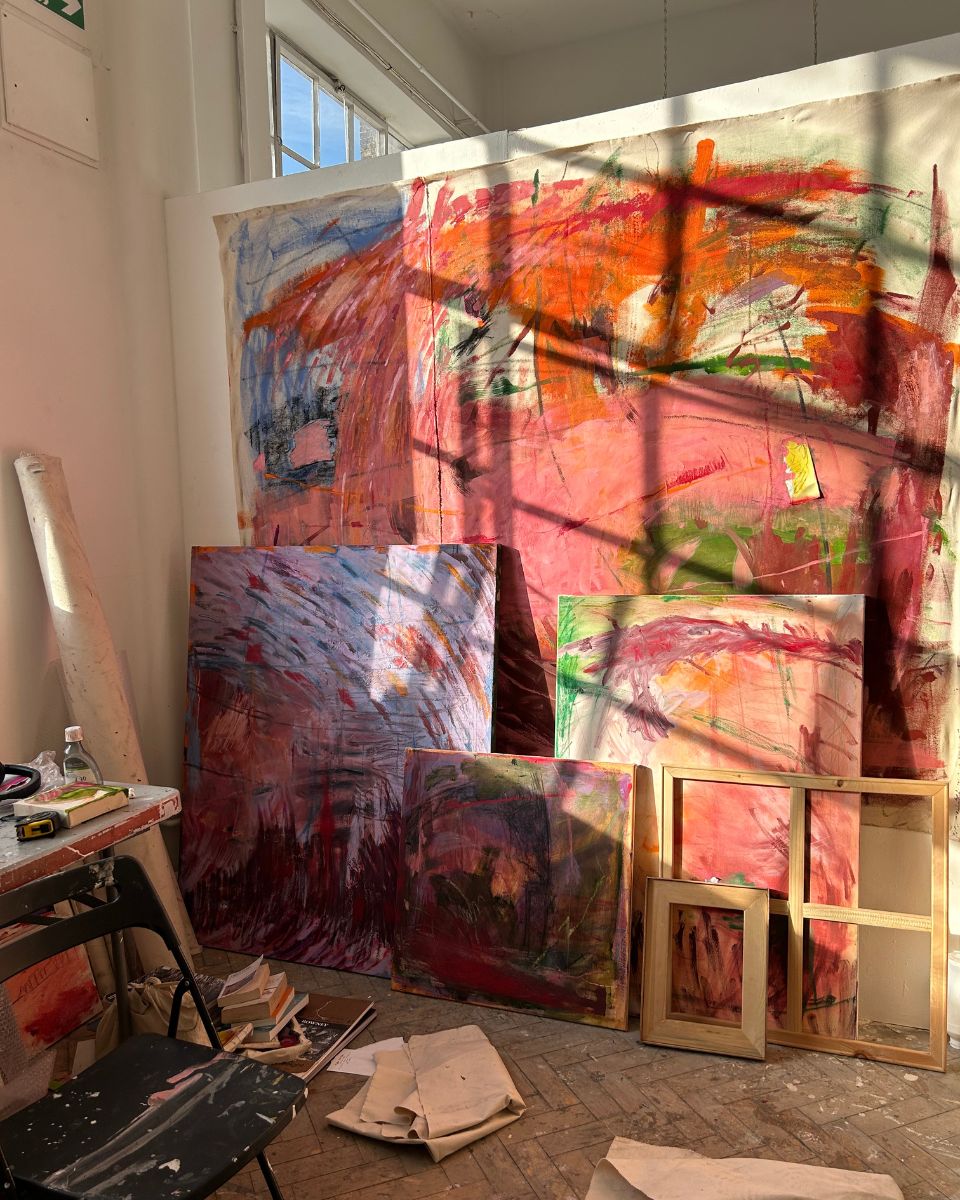 Large abstract expressionist oil paintings with pink, orange, and red tones resting against studio walls by Ellie Walker.