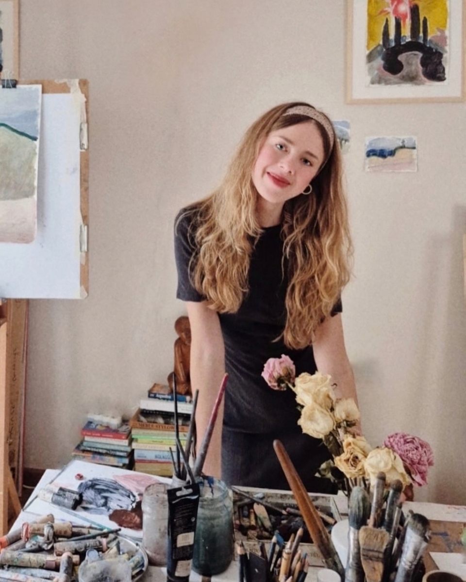 Portrait of artist Emilia Durka smiling in her studio, posing in front of her desk with art materials for Partnership Editions. 