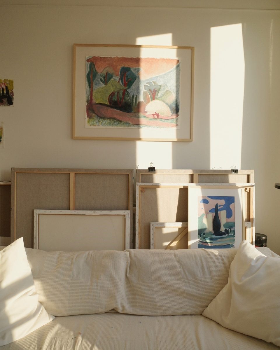 Carousel image of Emilia Durka’s home studio featuring a framed landscape painting mounted alongside unframed canvases for Partnership Editions.
