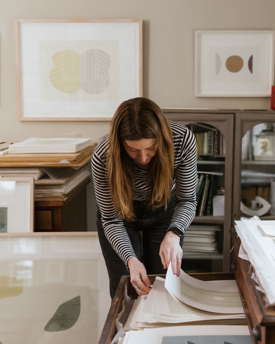 Artist Emma Lawrenson looking through a collection of handmade screenprints inside her printmaking studio.