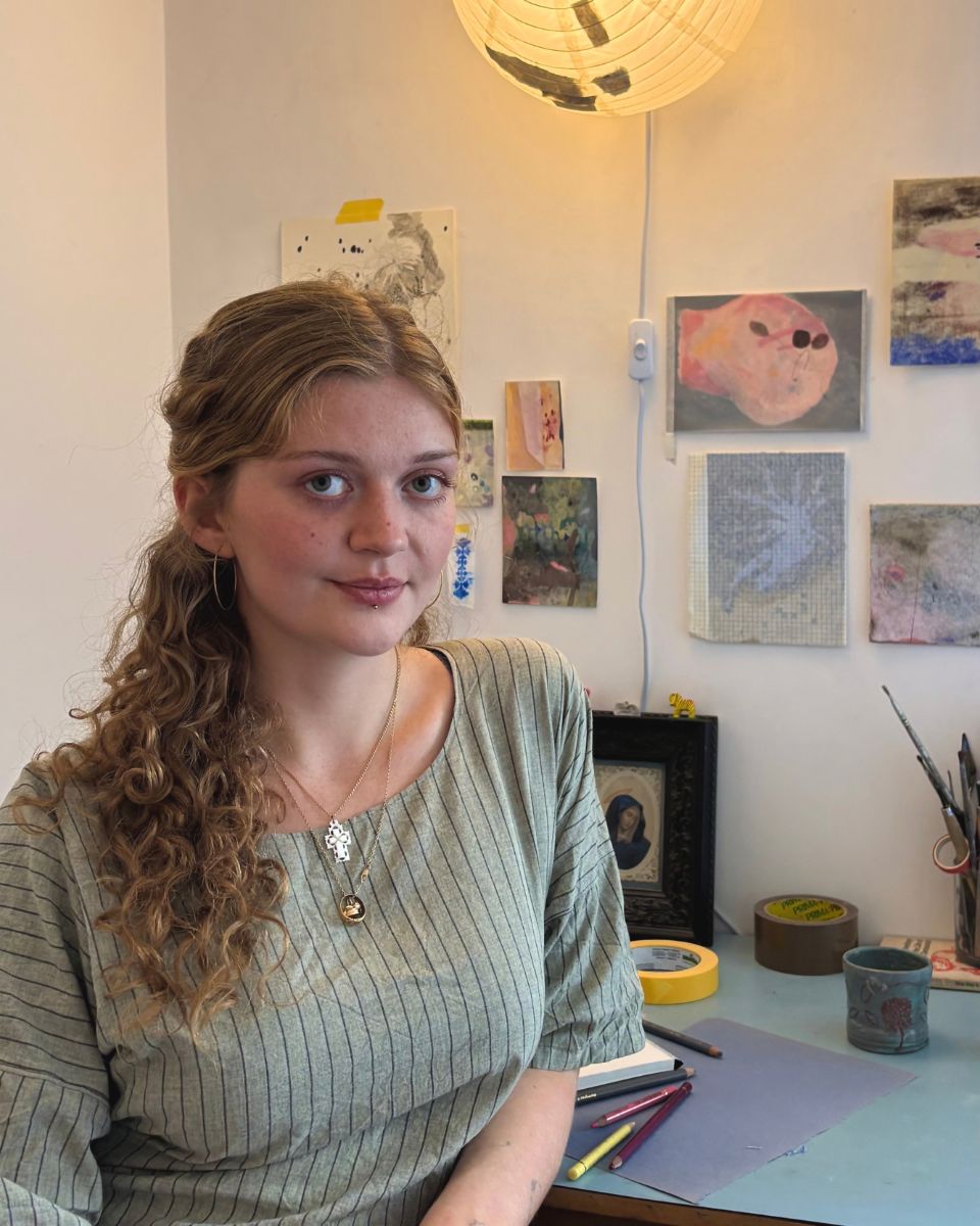 Portrait of British artist Esme McMillan-Scott sitting at her studio desk with coloured pencils and paper works for Partnership Editions.
