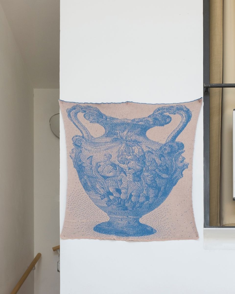 Close-up detail of a blue and cream knitted textile artwork depicting a classical urn motif by Eva Sajovic.