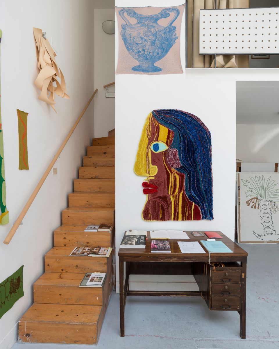 Colourful textile face profile artwork mounted above a desk by wooden stairs in Eva Sajovic's studio.