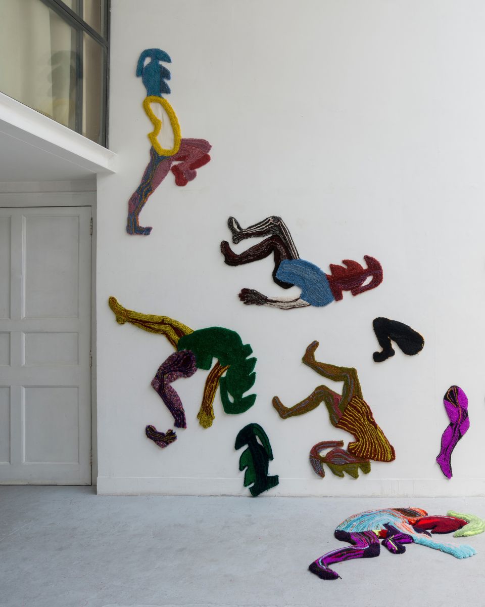 White gallery wall featuring an arrangement of colourful soft-sculptural textile figures by Eva Sajovic.
