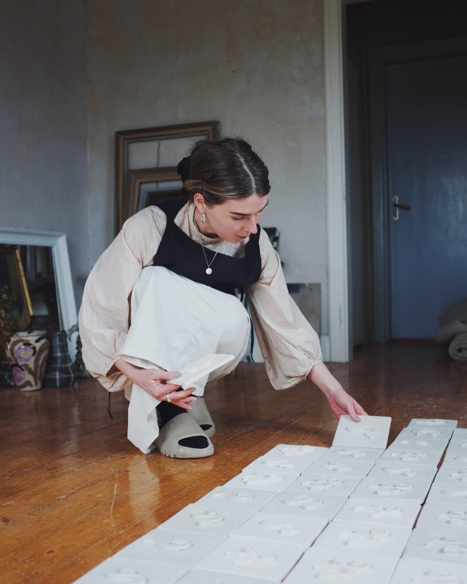 Carousel image of artist Fanny Schultz arranging handmade ceramic tiles on her studio floor for Partnership Editions.