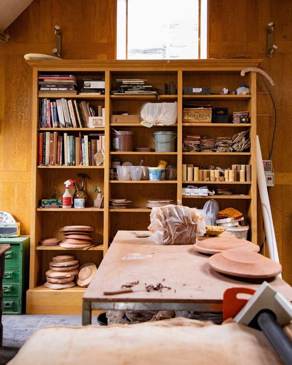 Carousel image of a studio work table and shelf showcasing slips, glazes, and botanical reference materials used by Freyja Lee for Partnership Editions.