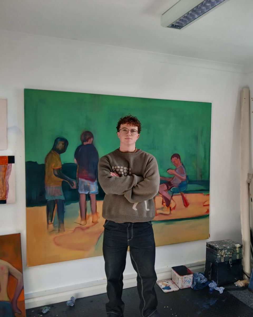 Artist George Marrington posing in his art studio in front of a large-scale figurative oil painting.