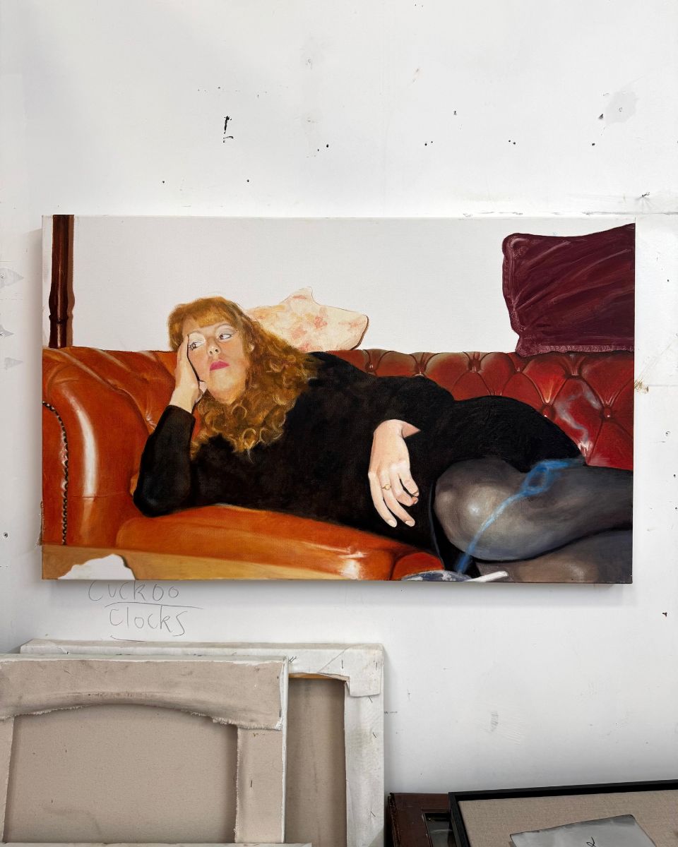 Oil painting on canvas depicting a woman with long red hair reclining on a tufted leather sofa by Georgie Huxley.