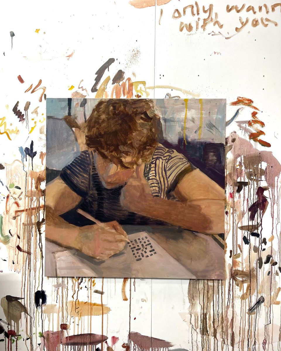Square oil painting on canvas of a person leaning over a desk pinned to a paint-splattered studio wall.