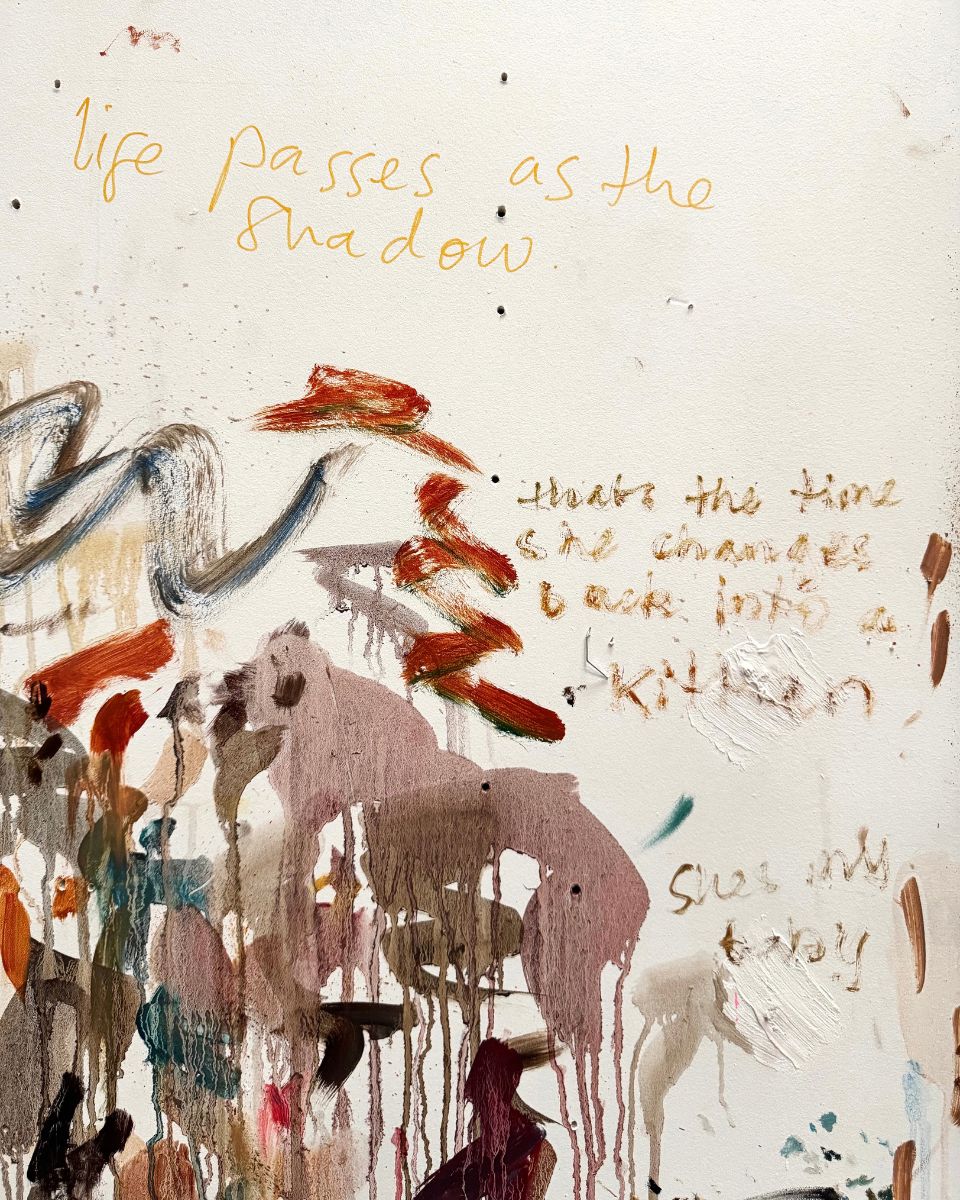 Close-up of handwritten notes, poetry quotes, and oil paint marks directly on a white studio wall.