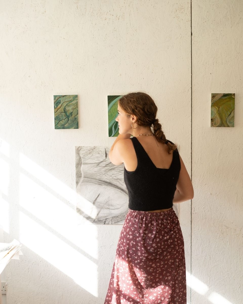 Artist Grace Crabtree captured in her studio standing before mounted contemporary landscape paintings for Partnership Editions.