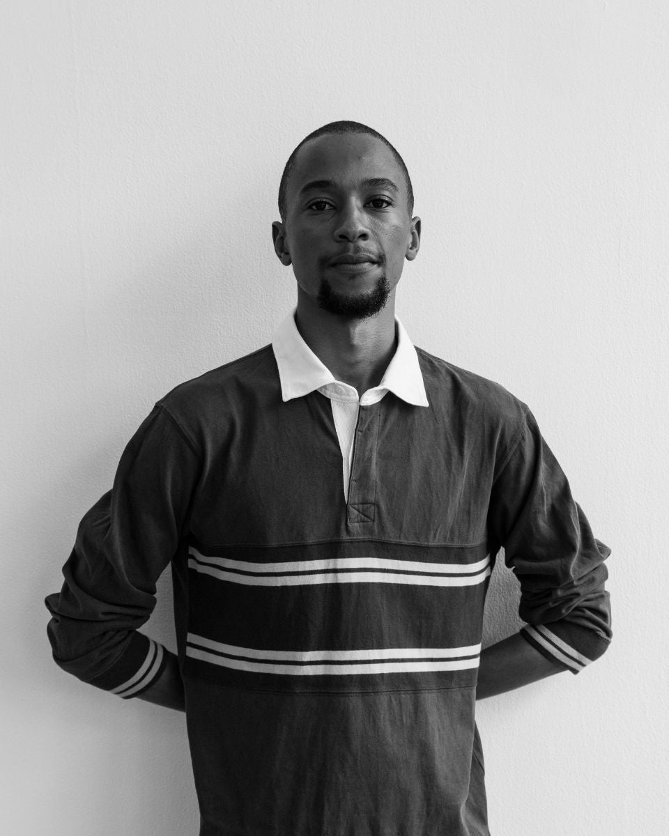Black and white portrait of artist Ian Gichohi wearing a striped rugby shirt in his studio for Partnership Editions.
