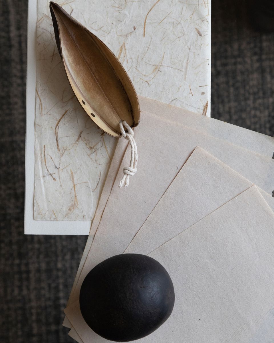 Close-up view of handmade textured paper sheets, seed pods, and natural materials on an artist desk.