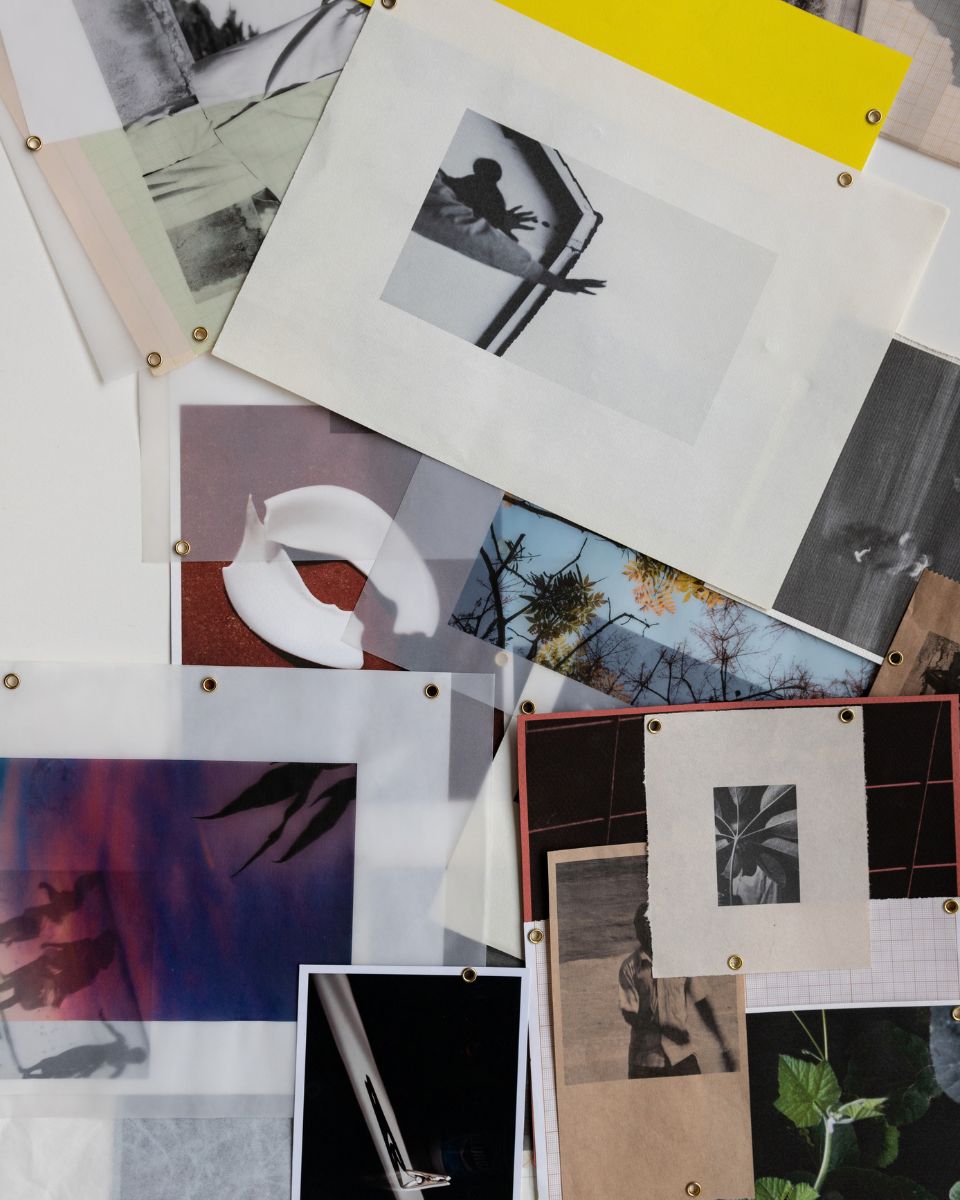 Overhead view of overlapping translucent paper, black-and-white prints, and photographic collages with metal eyelets.