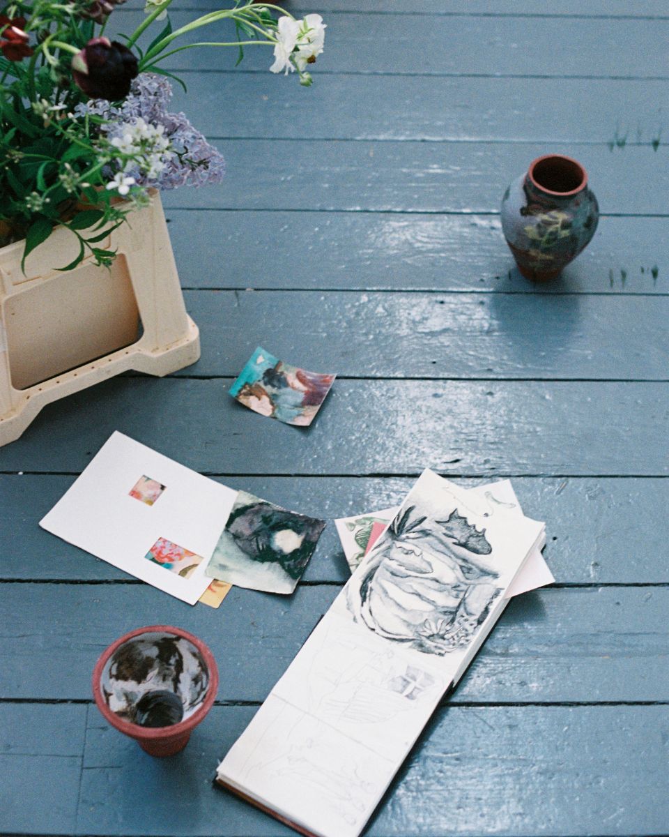 Imogen Richards’ sketches, hand-painted vases, and fresh flowers arranged across a blue-tinted wood floor.