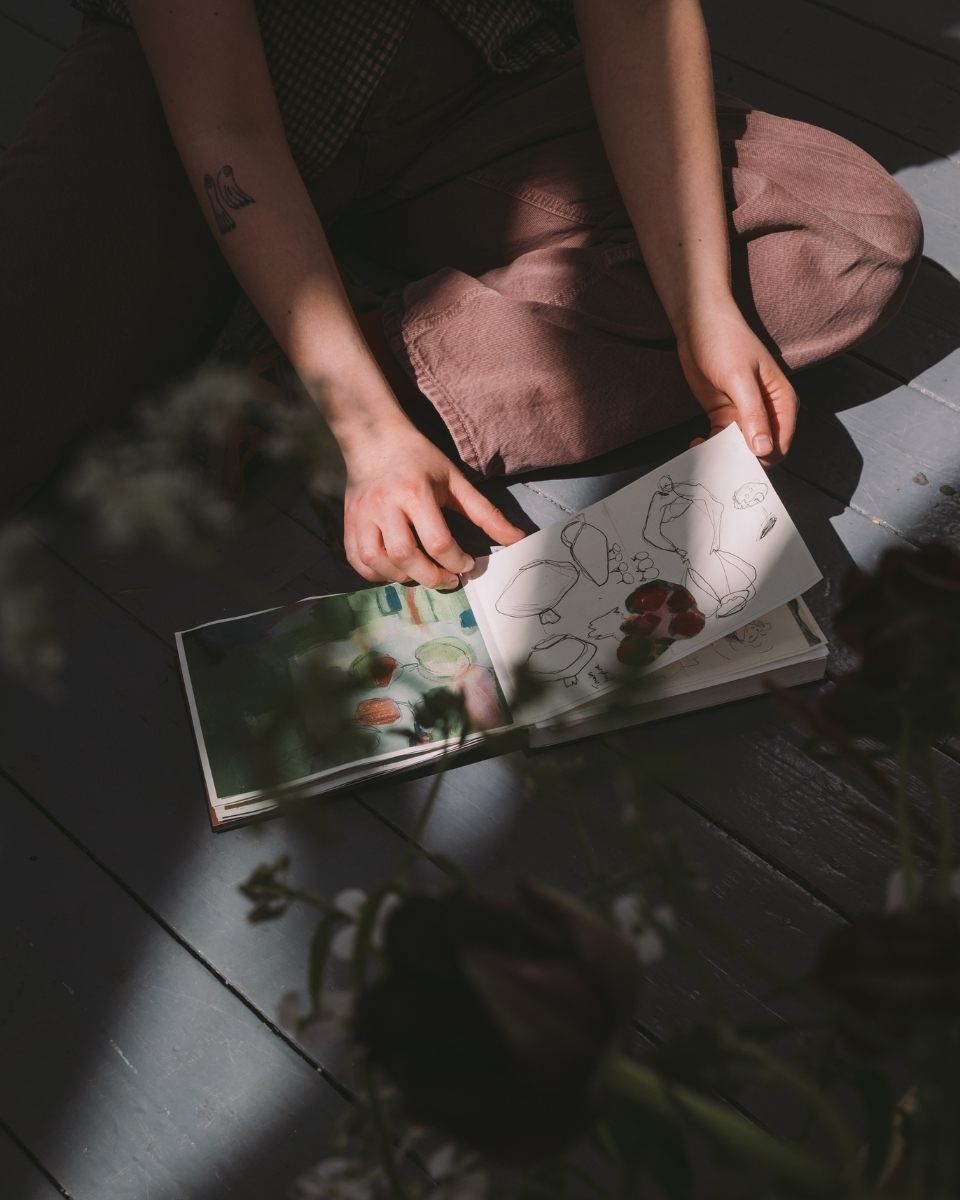 Close-up shot of artist Imogen Richards’ hands flipping through her paper sketchbook pages in the studio.
