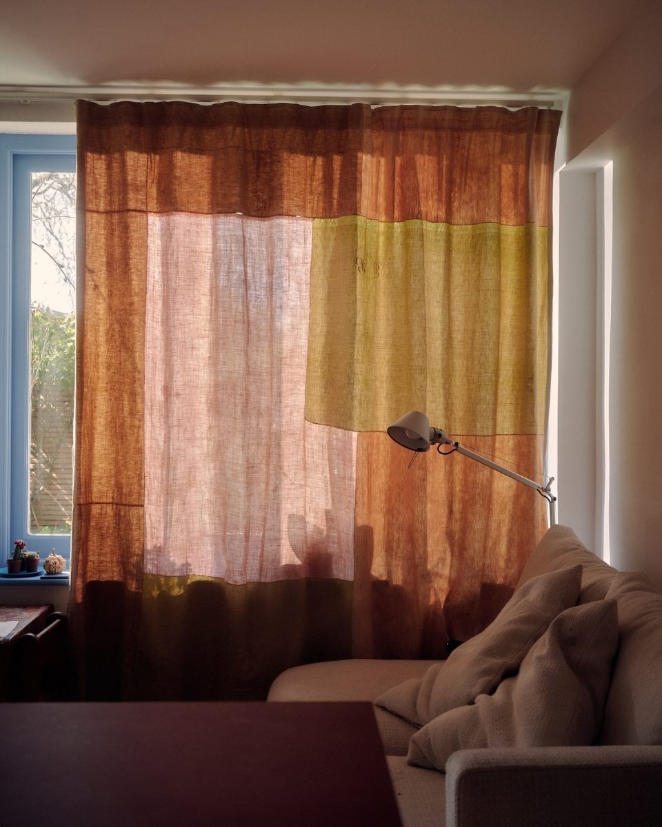 Carousel image of an Isabel Farchy patchwork textile curtain in use as a window treatment, filtering natural light in her home studio.