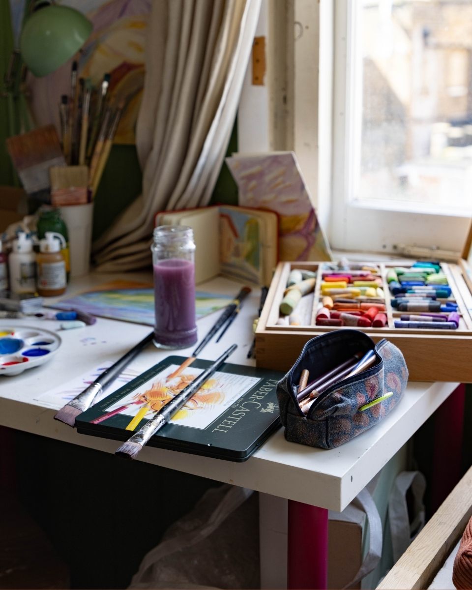 Detail shot of Isabel Garfield’s art materials, including wax crayons, pigment sticks, and watercolours on her studio desk for Partnership Editions.