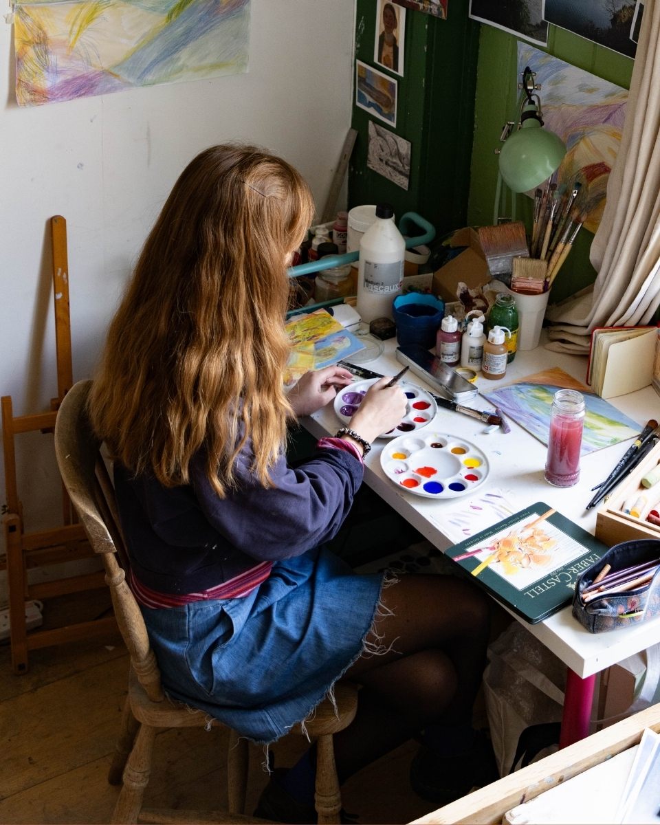 Isabel Garfield sitting at her studio desk, mixing bright pigment washes for a new series of works for Partnership Editions.
