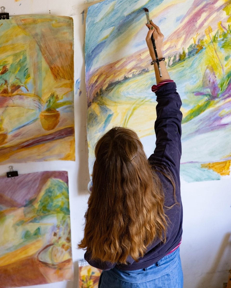 Close-up from behind of artist Isabel Garfield painting a gestural work on paper pinned to her studio wall.