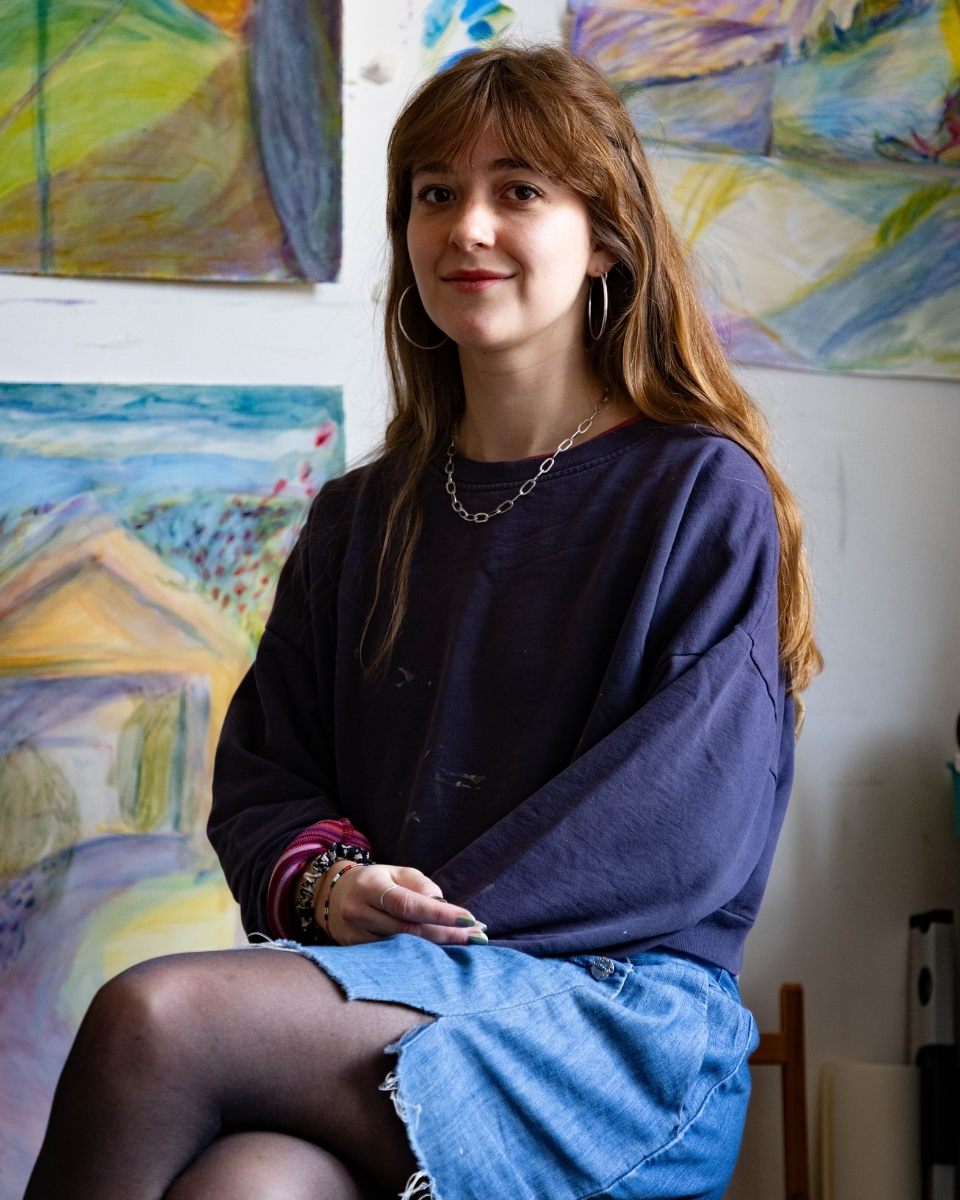 Seated portrait of artist Isabel Garfield in her studio in front of her expressive artworks.
