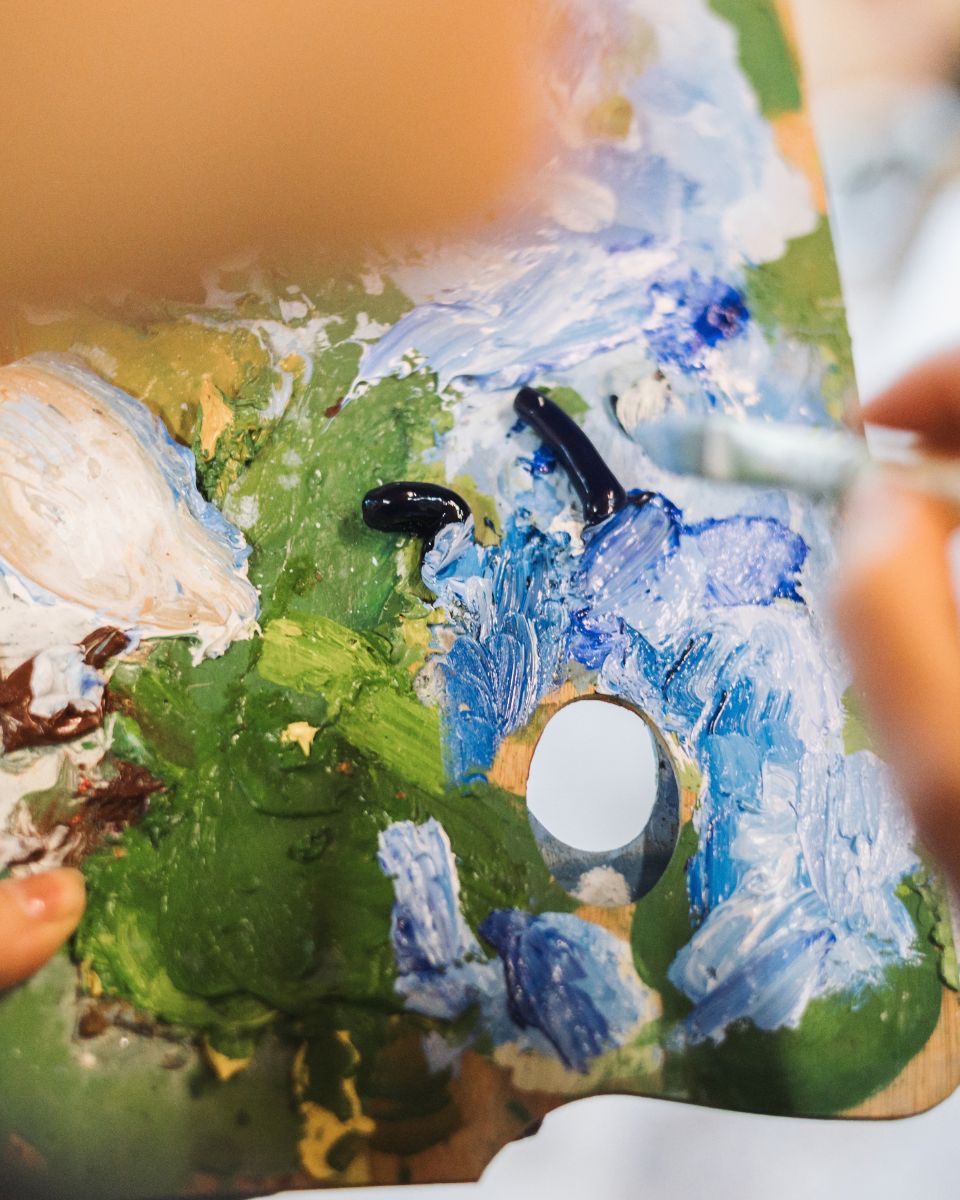 Close-up of a wooden artist palette covered in thick blue, green, and white oil paint mixes.