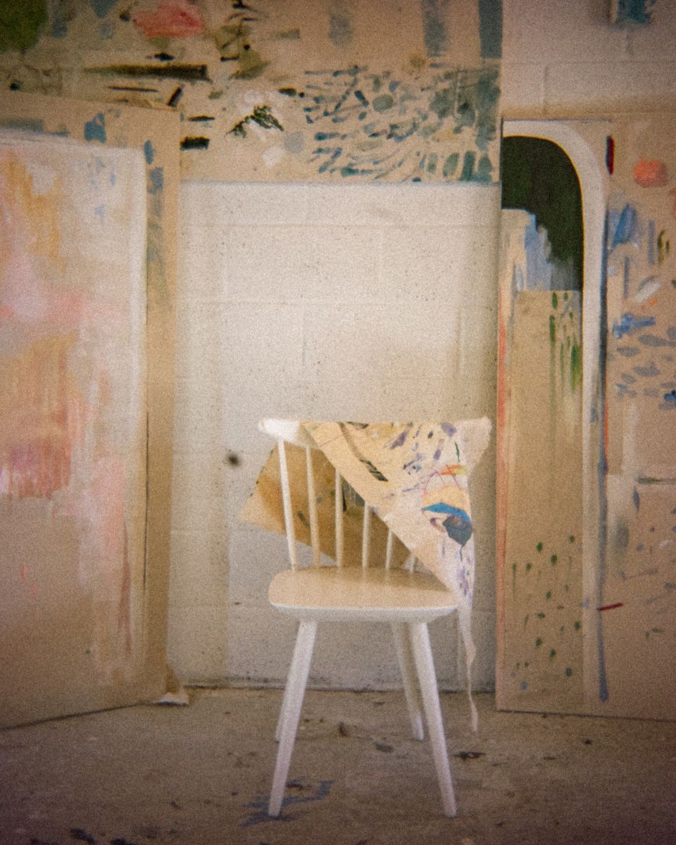 Small abstract painted canvas draped over a white wooden chair against studio wall mark-making.