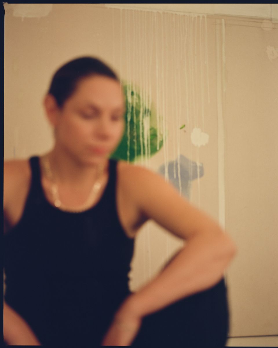 Atmospheric portrait of artist Ita Wooller wearing a black tank top in her art studio.