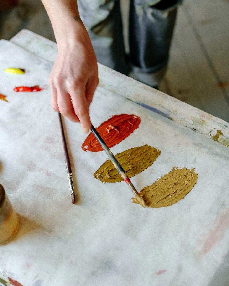 Close-up of artist Jay Harper’s hand mixing custom oil paint pigments on a palette for a new still life for Partnership Editions.