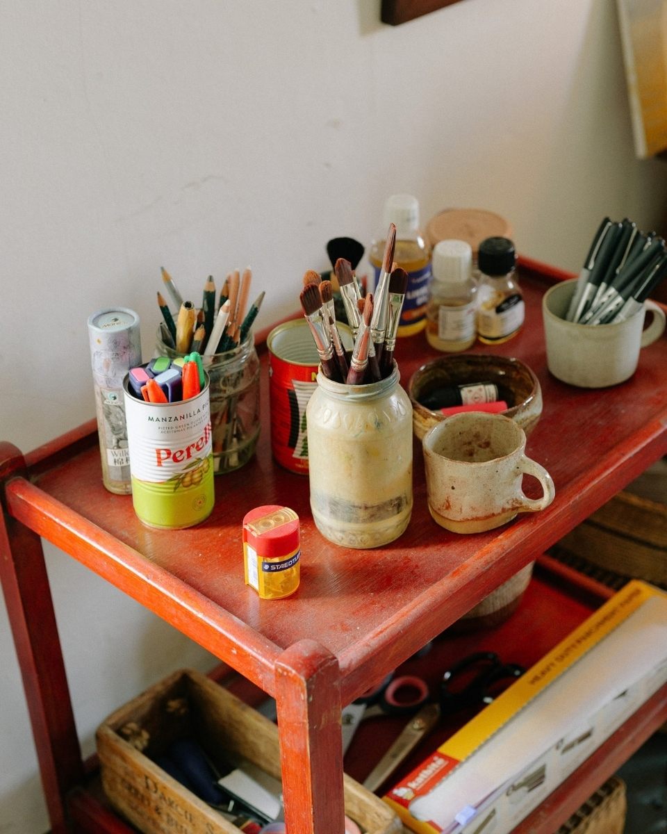 Detail shot of a signature red artist trolley in Jay Harper’s studio, organised with brushes, oil paints, and sketching pencils for Partnership Editions.
