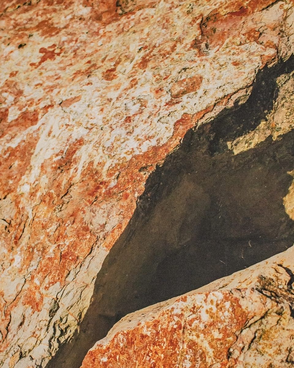 Close-up of a dramatic photograph by Jesse Williams, depicting a narrow light-filled gap between vibrant red rocks for Partnership Editions.