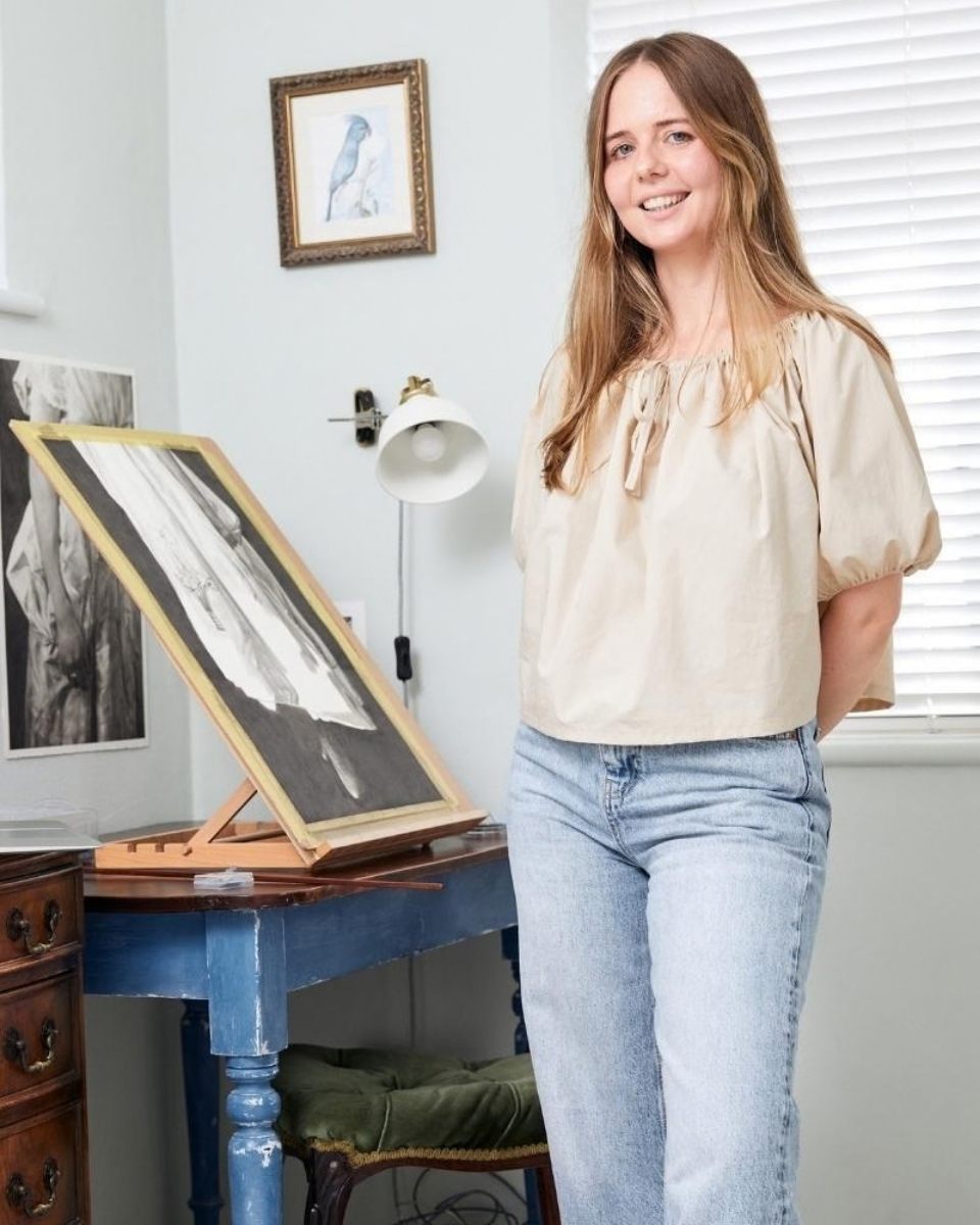 Artist Jo Dumpleton posing in her studio in front of a portrait drawing on her easel for Partnership Editions.