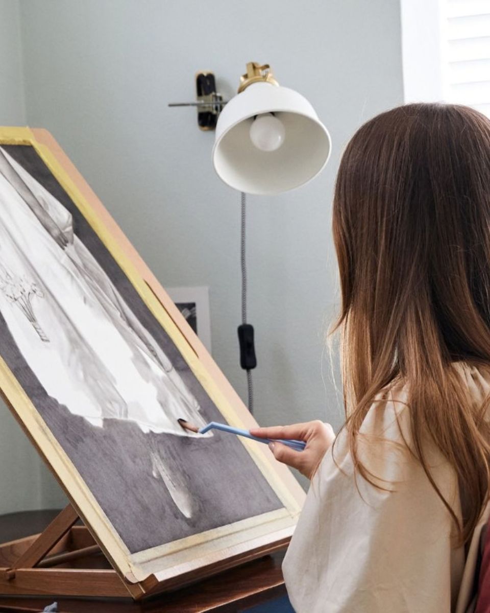 Close-up from behind of fine artist Jo Dumpleton drawing an intricate portrait piece in her studio.
