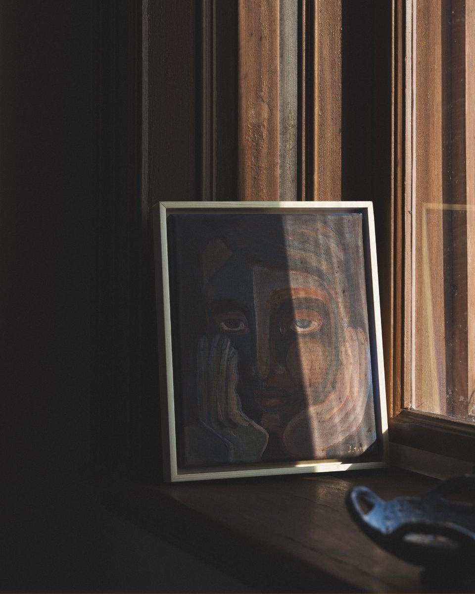 Close-up of a small framed Josefin Tolstoy painting on a windowsill illuminated by soft natural light.