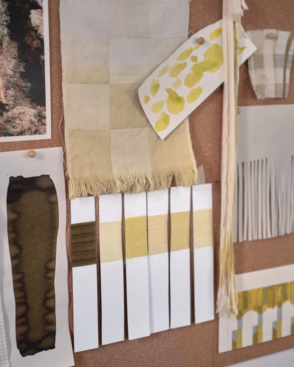 Close-up of cork moodboard with woven check swatches, yarn wrappings, and olive green colour test strips.